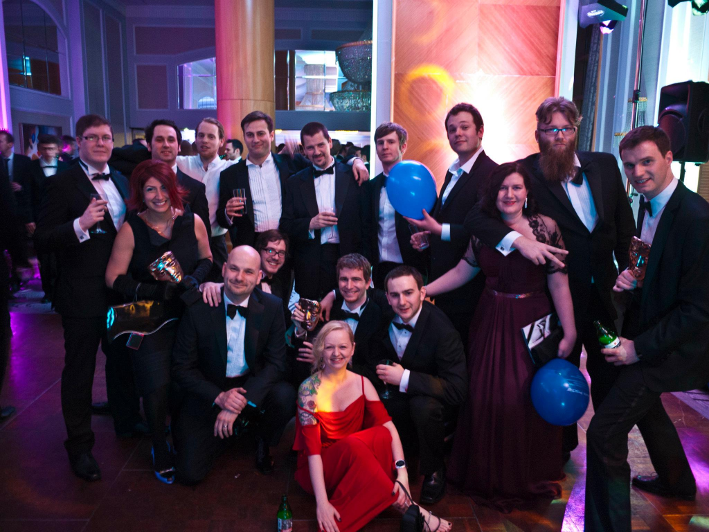 Photograph of game developers dressed as smartly as is possible, in a ballroom in the London Hilton. 

11 standing along the back, the other 6 of the team squatting in front. 

3 of the 4 founders holding one of the 3 duplicate trophies awarded to us.

Mixture of happy and awkward expressions.